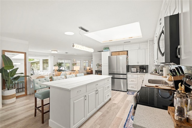 1112 Montezuma Dr, Bradenton, FL 34209 - kitchen with stainless steel appliances, a center island, light wood-style flooring, and white cabinets