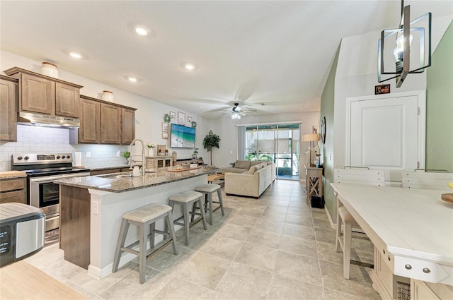 8676 Ice Wine St, Sarasota, FL 34238 - kitchen with electric range, a kitchen breakfast bar, under cabinet range hood, a ceiling fan, and stone countertops