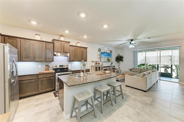 8676 Ice Wine St, Sarasota, FL 34238 - kitchen featuring appliances with stainless steel finishes, a breakfast bar area, under cabinet range hood, tasteful backsplash, and stone countertops