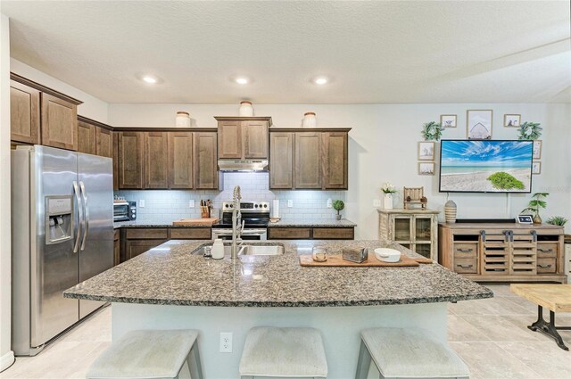 8676 Ice Wine St, Sarasota, FL 34238 - kitchen with appliances with stainless steel finishes, under cabinet range hood, dark stone counters, backsplash, and an island with sink