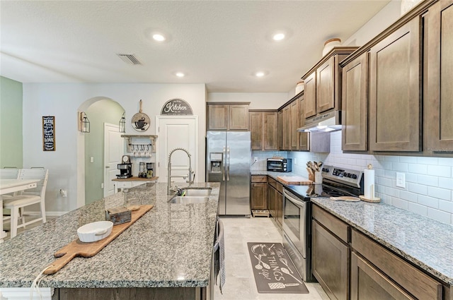 8676 Ice Wine St, Sarasota, FL 34238 - kitchen featuring appliances with stainless steel finishes, arched walkways, under cabinet range hood, a large island with sink, and decorative backsplash
