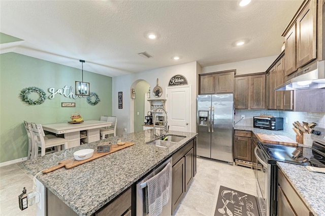8676 Ice Wine St, Sarasota, FL 34238 - kitchen featuring appliances with stainless steel finishes, under cabinet range hood, arched walkways, light stone counters, and an island with sink