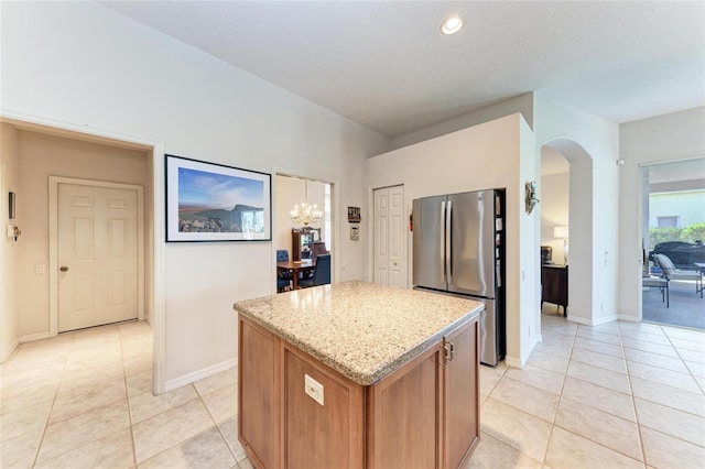 11915 Oak Ridge Dr, Parrish, FL 34219 - kitchen with freestanding refrigerator, a kitchen island, arched walkways, light tile patterned floors, and light stone countertops