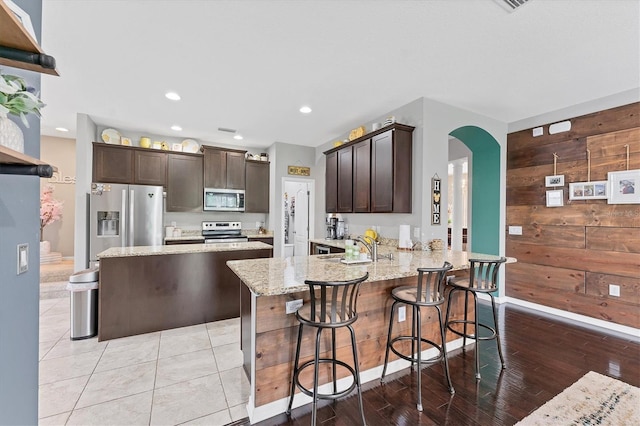 9123 Raes Creek Pl, Palmetto, FL 34221 - kitchen featuring stainless steel appliances, dark brown cabinets, arched walkways, light stone counters, and recessed lighting