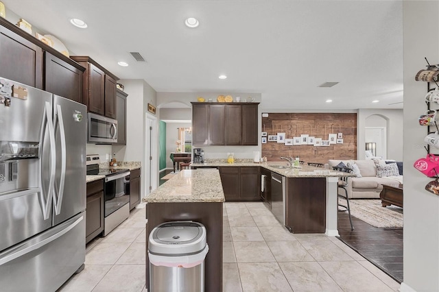 9123 Raes Creek Pl, Palmetto, FL 34221 - kitchen with appliances with stainless steel finishes, arched walkways, dark brown cabinetry, a center island, and recessed lighting