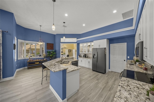 8924 Misty Creek Dr, Sarasota, FL 34241 - kitchen with appliances with stainless steel finishes, white cabinets, a kitchen breakfast bar, light stone countertops, and light wood finished floors