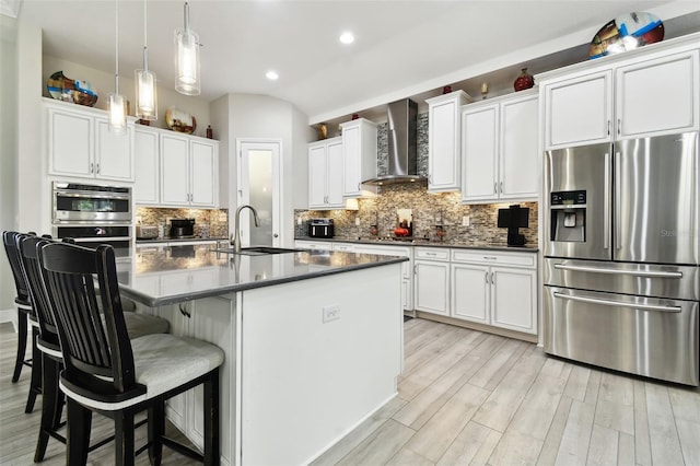 5802 Alabaster Stone Ln, Apollo Beach, FL 33572 - kitchen featuring appliances with stainless steel finishes, wall chimney exhaust hood, dark countertops, light wood-type flooring, and tasteful backsplash