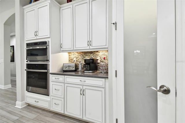 5802 Alabaster Stone Ln, Apollo Beach, FL 33572 - kitchen featuring stainless steel double oven, arched walkways, dark countertops, backsplash, and light wood-type flooring