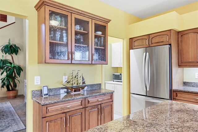 175 Inlets Blvd Unit 175, Nokomis, FL 34275 - kitchen with freestanding refrigerator, brown cabinetry, light stone countertops, and glass insert cabinets