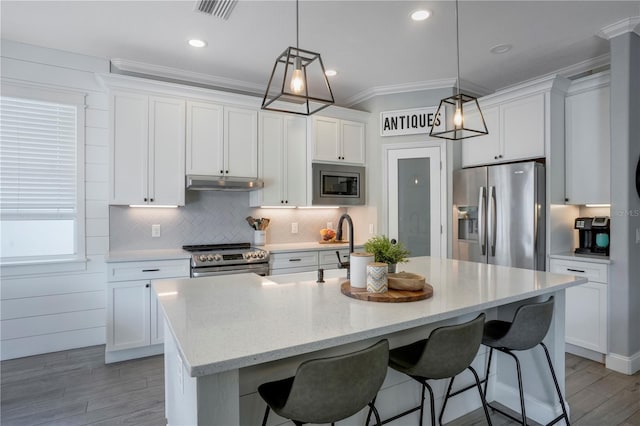 5419 Lakehurst Ct, Palmetto, FL 34221 - kitchen featuring appliances with stainless steel finishes, under cabinet range hood, a breakfast bar, white cabinets, and crown molding