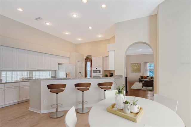 5839 Los Verdes Ct, Bradenton, FL 34210 - kitchen featuring white appliances, arched walkways, a peninsula, a kitchen bar, and white cabinets