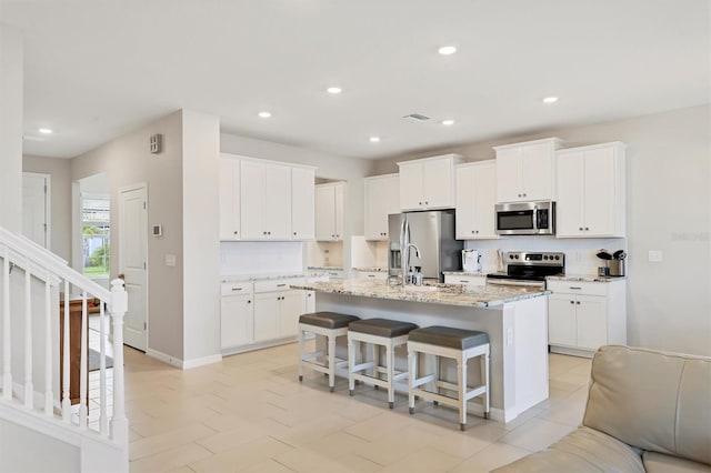 12564 Night View Dr, Sarasota, FL 34238 - kitchen with stainless steel appliances, a kitchen bar, white cabinets, a center island with sink, and recessed lighting