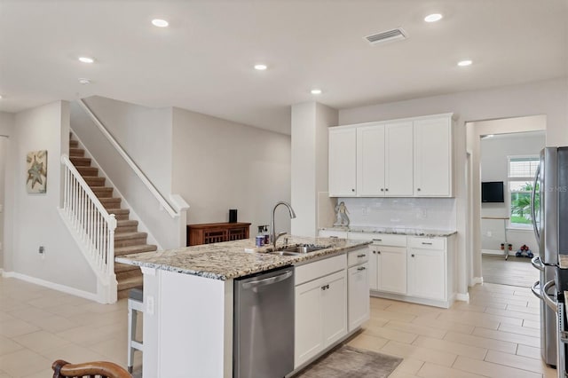 12564 Night View Dr, Sarasota, FL 34238 - kitchen with appliances with stainless steel finishes, light stone counters, a kitchen island with sink, white cabinetry, and decorative backsplash