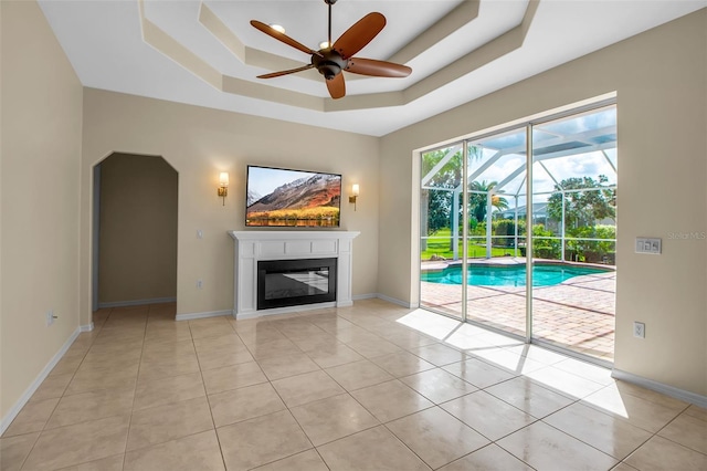 2148 Date Palm Way, Venice, FL 34292 - unfurnished living room featuring ceiling fan, a raised ceiling, light tile patterned flooring, a sunroom, and a glass covered fireplace