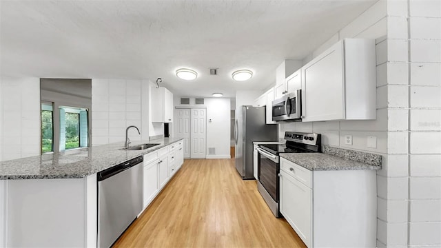 4455 Emerald Ridge Dr, Sarasota, FL 34233 - kitchen featuring stainless steel appliances, a peninsula, light wood-style flooring, white cabinetry, and stone counters