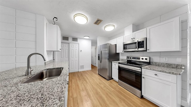 4455 Emerald Ridge Dr, Sarasota, FL 34233 - kitchen featuring stainless steel appliances, light wood-type flooring, white cabinetry, light stone counters, and backsplash