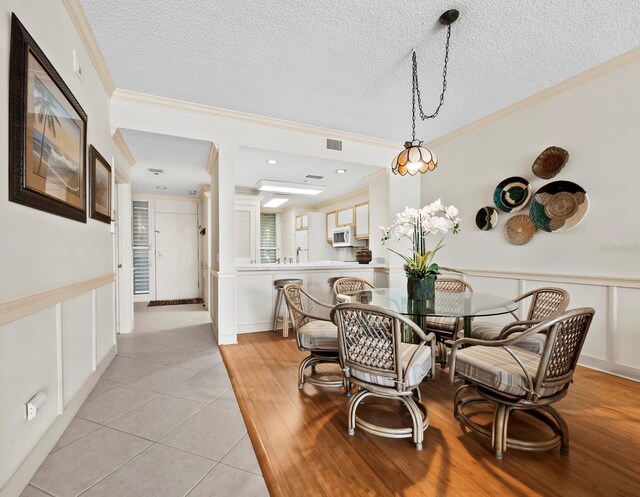 615 Dream Island Pl Unit 105, Longboat Key, FL 34228 - dining area featuring crown molding, a textured ceiling, wainscoting, light wood-style floors, and a decorative wall