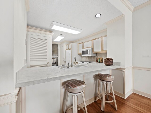 615 Dream Island Pl Unit 105, Longboat Key, FL 34228 - kitchen with white appliances, tile counters, crown molding, a peninsula, and wood finished floors