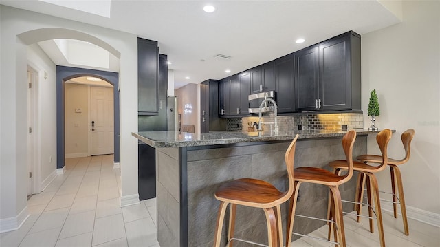 1921 Monte Carlo Dr Unit 302, Sarasota, FL 34231 - kitchen with stainless steel microwave, stone countertops, arched walkways, backsplash, and a peninsula