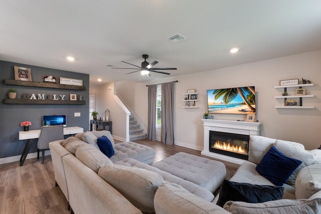 8985 Royal River Cir, Parrish, FL 34219 - living area featuring a glass covered fireplace, wood finished floors, ceiling fan, recessed lighting, and stairs