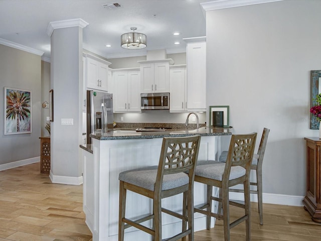 7840 34th Ave W Unit 303, Bradenton, FL 34209 - kitchen featuring stainless steel appliances, a breakfast bar, light wood-style floors, white cabinets, and ornamental molding