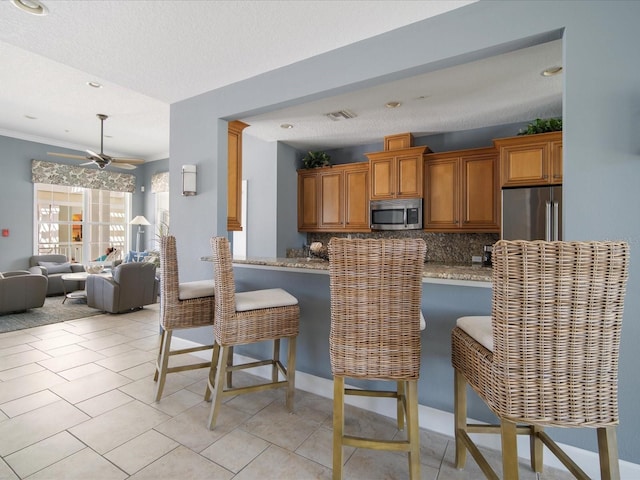 7840 34th Ave W Unit 303, Bradenton, FL 34209 - kitchen featuring appliances with stainless steel finishes, brown cabinetry, tasteful backsplash, a breakfast bar, and a textured ceiling