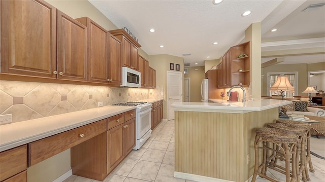 7012 Treymore Ct, Sarasota, FL 34243 - kitchen with white appliances, a breakfast bar area, backsplash, brown cabinets, and a peninsula