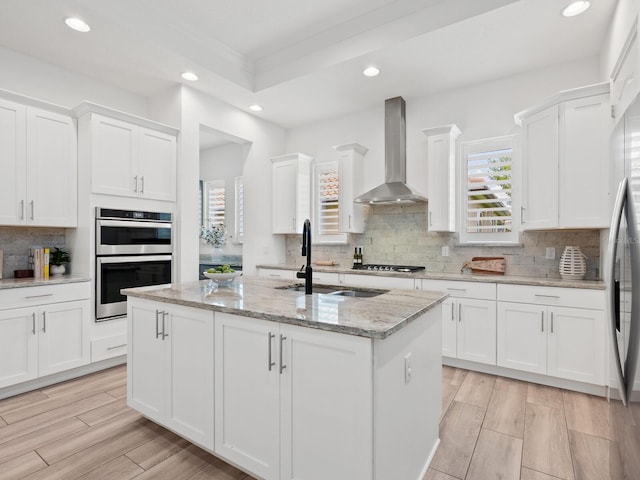 10120 Carnoustie Pl, Bradenton, FL 34211 - kitchen with wall chimney exhaust hood, stainless steel double oven, a center island with sink, white cabinets, and recessed lighting