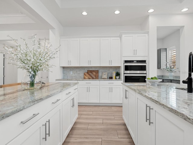 10120 Carnoustie Pl, Bradenton, FL 34211 - kitchen featuring stainless steel double oven, tasteful backsplash, recessed lighting, white cabinetry, and light stone countertops