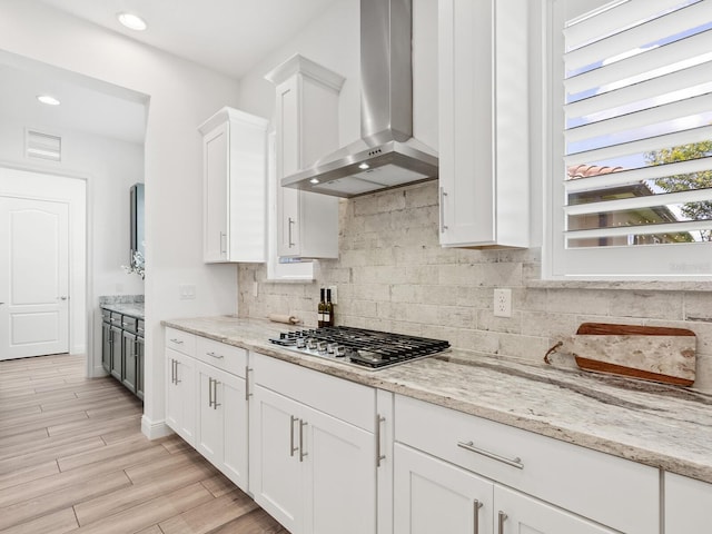 10120 Carnoustie Pl, Bradenton, FL 34211 - kitchen featuring wall chimney exhaust hood, stainless steel gas cooktop, decorative backsplash, white cabinetry, and light stone countertops