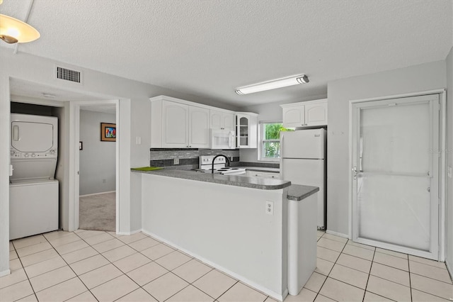 25100 Sandhill Blvd Unit 104G, Punta Gorda, FL 33983 - kitchen with white appliances, stacked washer and clothes dryer, light tile patterned flooring, a peninsula, and a textured ceiling