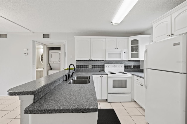 25100 Sandhill Blvd Unit 104G, Punta Gorda, FL 33983 - kitchen featuring white appliances, stacked washing machine and dryer, light tile patterned floors, dark countertops, and white cabinetry