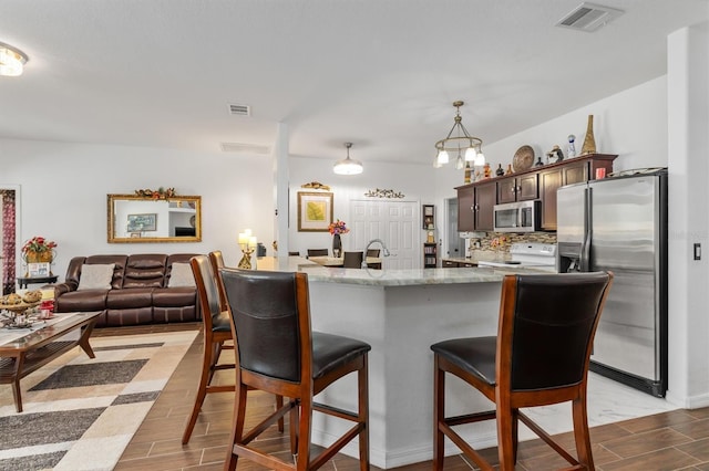 25324 Alicante Dr, Punta Gorda, FL 33955 - kitchen featuring stainless steel appliances, a breakfast bar area, light wood finished floors, dark brown cabinets, and light stone counters