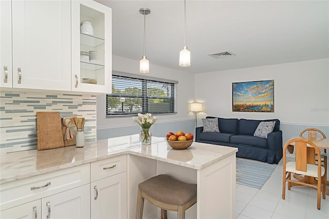 1400 1st Ave W Unit 103, Bradenton, FL 34205 - kitchen featuring a wainscoted wall, white cabinets, a peninsula, light tile patterned floors, and backsplash