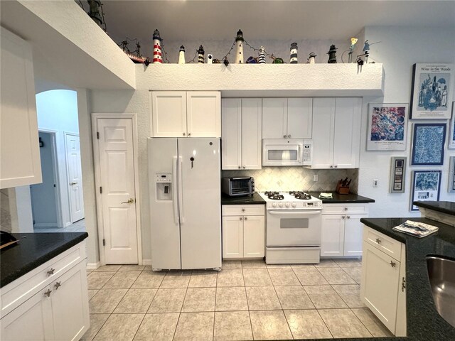 8616 15th Ave NW, Bradenton, FL 34209 - kitchen with white appliances, decorative backsplash, light tile patterned floors, white cabinets, and dark countertops