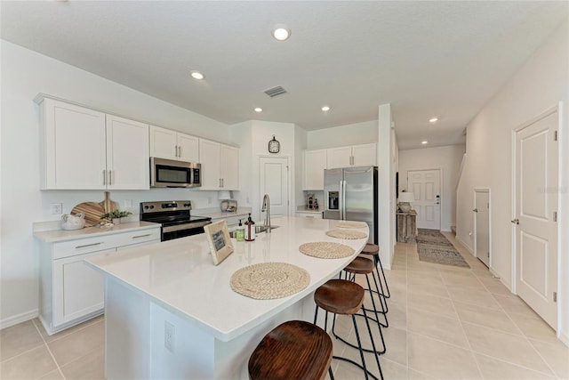 5711 Archipelago St, Nokomis, FL 34275 - kitchen with appliances with stainless steel finishes, a kitchen breakfast bar, light tile patterned floors, an island with sink, and white cabinets