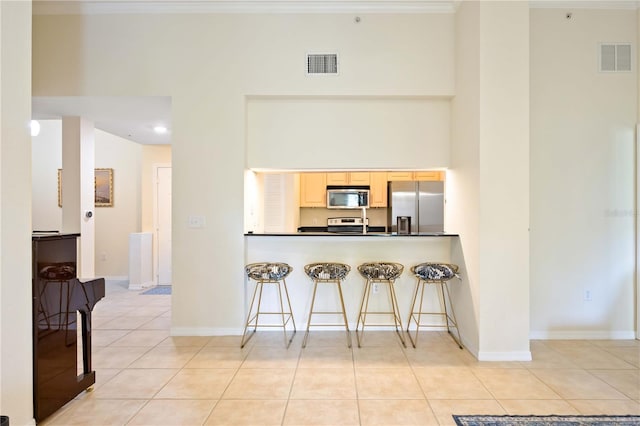 1064 N Tamiami Trl Unit 1125, Sarasota, FL 34236 - kitchen featuring stainless steel appliances, light brown cabinetry, light tile patterned flooring, dark countertops, and a kitchen bar