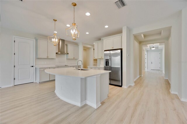 918 Fernleaf Run, Bradenton, FL 34212 - kitchen with stainless steel fridge, wall chimney exhaust hood, light wood-style flooring, light countertops, and a center island with sink
