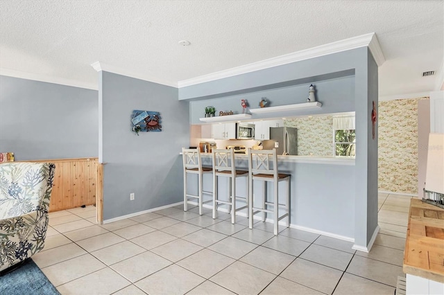 3810 75th St W Unit 128, Bradenton, FL 34209 - kitchen with appliances with stainless steel finishes, ornamental molding, a textured ceiling, tile patterned flooring, and a kitchen breakfast bar