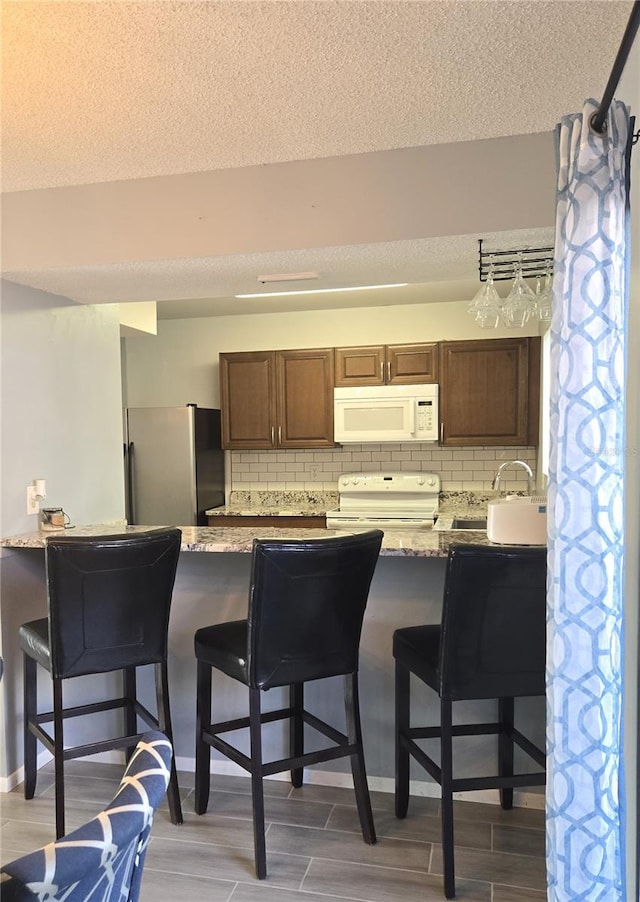 4001 Beneva Rd Unit 319, Sarasota, FL 34233 - kitchen featuring white appliances, backsplash, a textured ceiling, a kitchen bar, and light stone counters