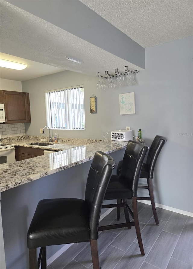 4001 Beneva Rd Unit 319, Sarasota, FL 34233 - kitchen featuring white appliances, a kitchen bar, a textured ceiling, light stone countertops, and a peninsula