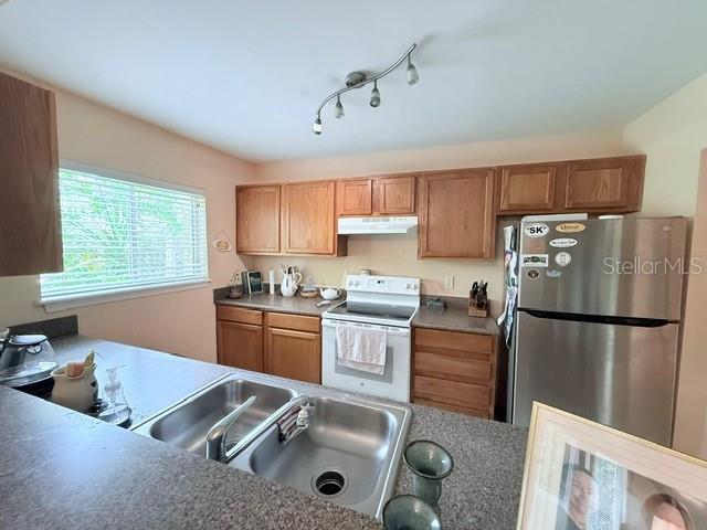 1959 Toucan Way Unit 206, Sarasota, FL 34232 - kitchen with freestanding refrigerator, white range with electric stovetop, under cabinet range hood, and brown cabinetry