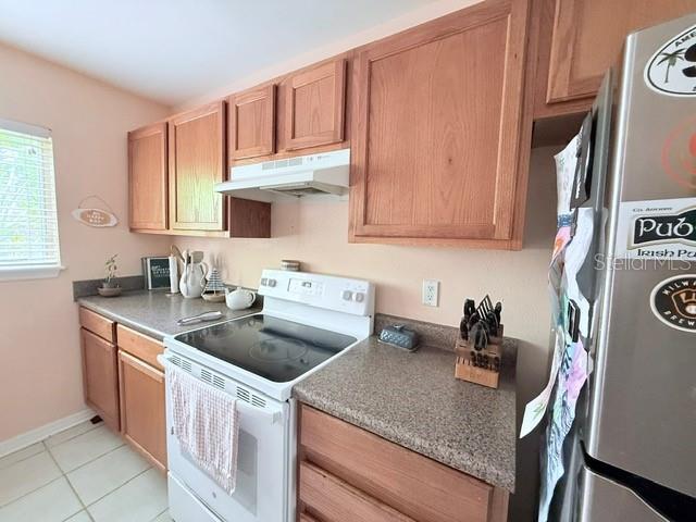 1959 Toucan Way Unit 206, Sarasota, FL 34232 - kitchen featuring white electric range, freestanding refrigerator, under cabinet range hood, and light tile patterned floors