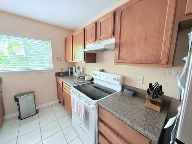 1959 Toucan Way Unit 206, Sarasota, FL 34232 - kitchen featuring white electric range oven, under cabinet range hood, freestanding refrigerator, light tile patterned floors, and brown cabinets
