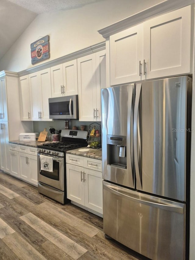 15917 Mercott Ct, Clermont, FL 34714 - kitchen featuring appliances with stainless steel finishes, vaulted ceiling, dark wood-style floors, white cabinetry, and dark stone counters