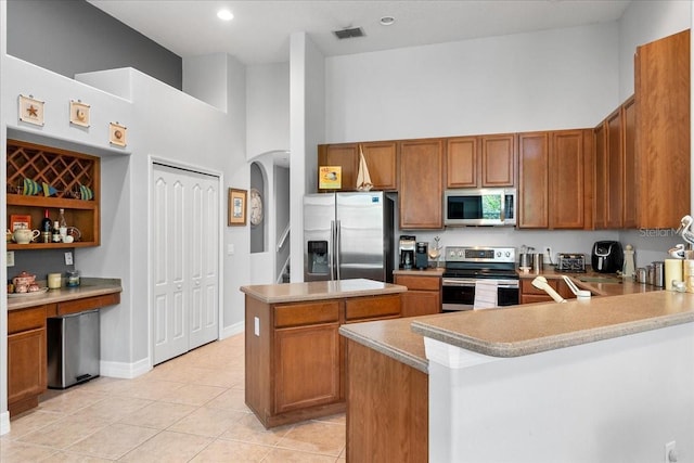4013 Greystone Dr, Clermont, FL 34711 - kitchen featuring stainless steel appliances, a high ceiling, brown cabinets, light tile patterned floors, and a center island