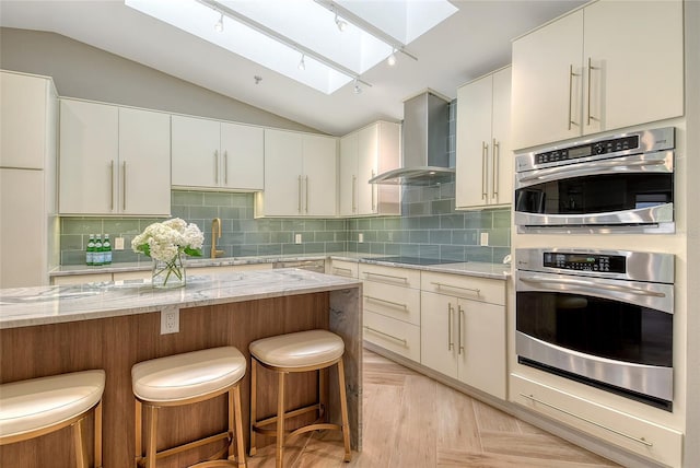2103 Harbourside Dr Unit 1102, Longboat Key, FL 34228 - kitchen with a skylight, wall chimney exhaust hood, double oven, a kitchen bar, and light stone countertops