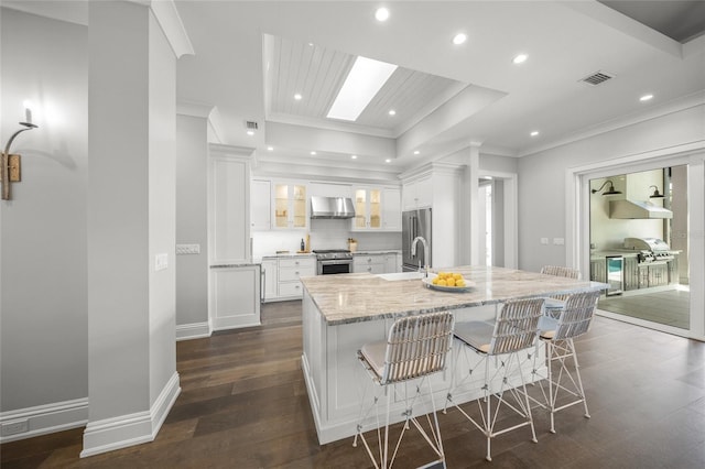 5569 Cape Leyte Dr, Sarasota, FL 34242 - kitchen with wall chimney range hood, dark wood-style flooring, white cabinets, stainless steel appliances, and ornamental molding