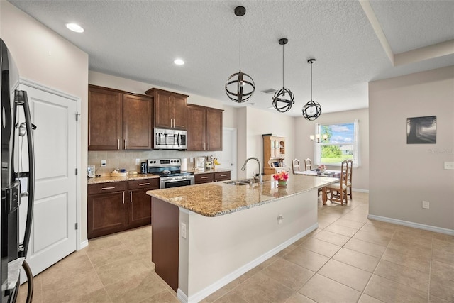 226 Tapa Parish Run, Bradenton, FL 34212 - kitchen with stainless steel appliances, a textured ceiling, light tile patterned floors, light stone counters, and an island with sink