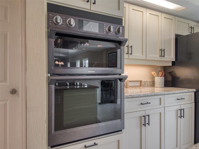 123 Tidy Island Blvd, Bradenton, FL 34210 - kitchen with double oven, freestanding refrigerator, white cabinetry, and light stone countertops